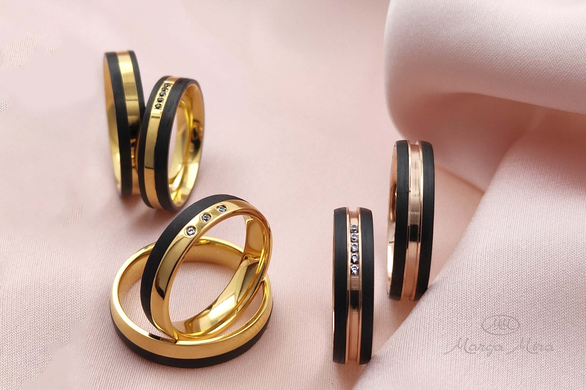 tres pares de alianzas de oro y carbono sobre una tela de color rosado. seis anillos de bodas de oro amarillo y carbono negro